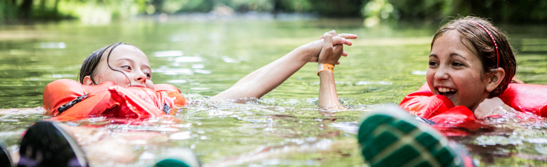 two girls floating in a river while holding hands and wearing life jackets