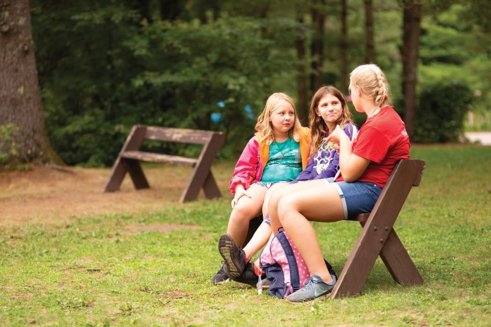 Camp counselor siting on a bench with two campers, talking