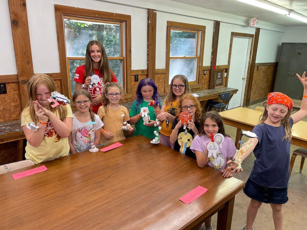Eight campers and one camp counselor show their craft projects