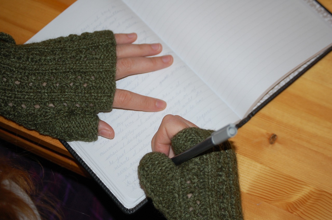 child's hands in fingerless gloves writing in a journal