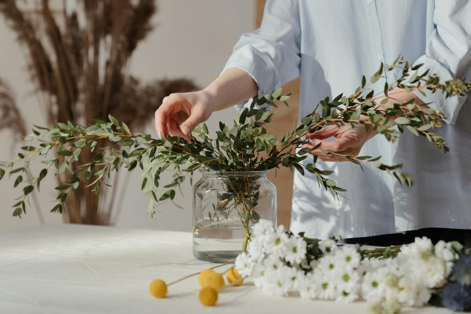 person's hands arranging plants in a wide jar with cut flowers nearby