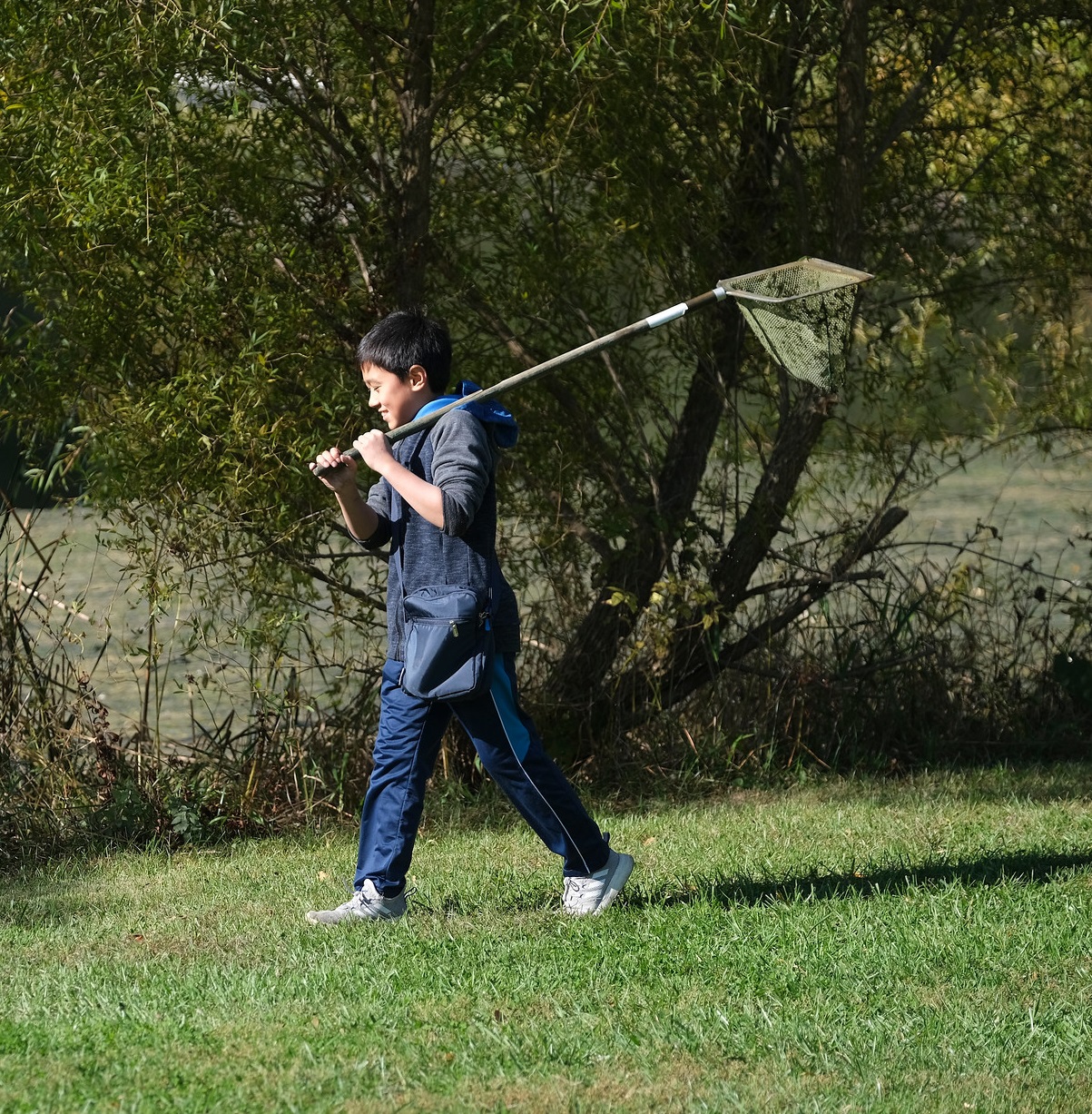 boy walking in the grass with a scoop net over his shoulder
