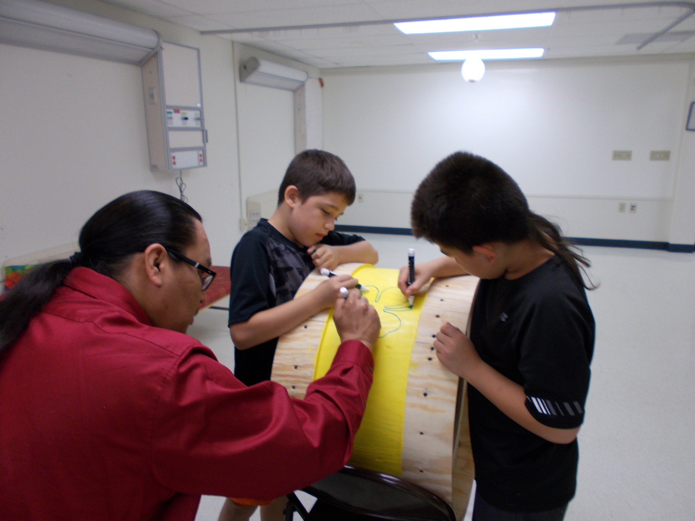 Two youth and an adult drawing on a drum