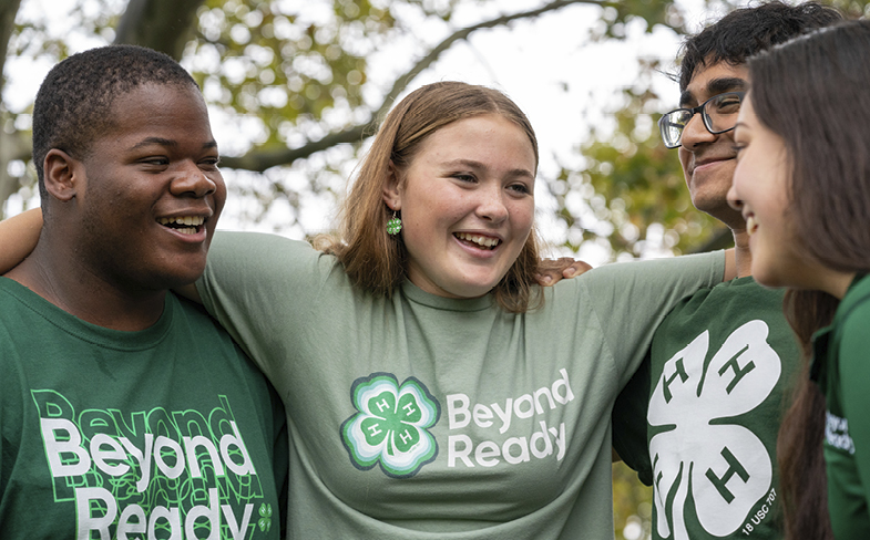 Four smiling young people stand close to each other outside.