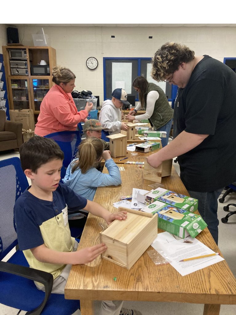 4-H youth and adults make birdhouses at a long table
