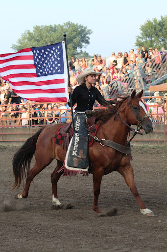 A person riding a horse while carrying the American flag during the national anthem.
