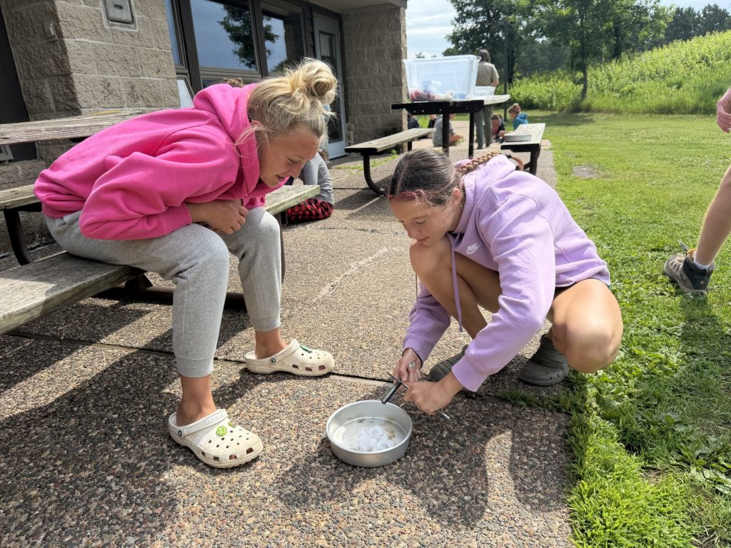 Two youth at Outpost Camp do a nature activity with a metal bowl.