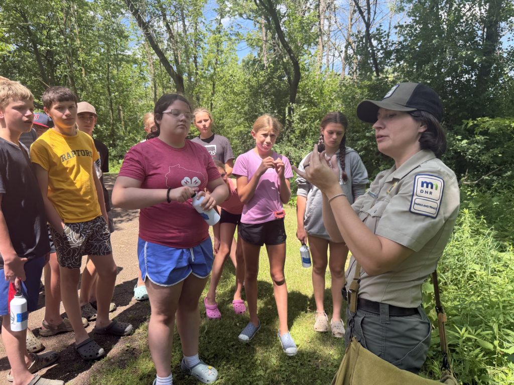Youth at Outpost Camp listen to Naturalist Elizabeth Nelson talk about a nut from a tree.